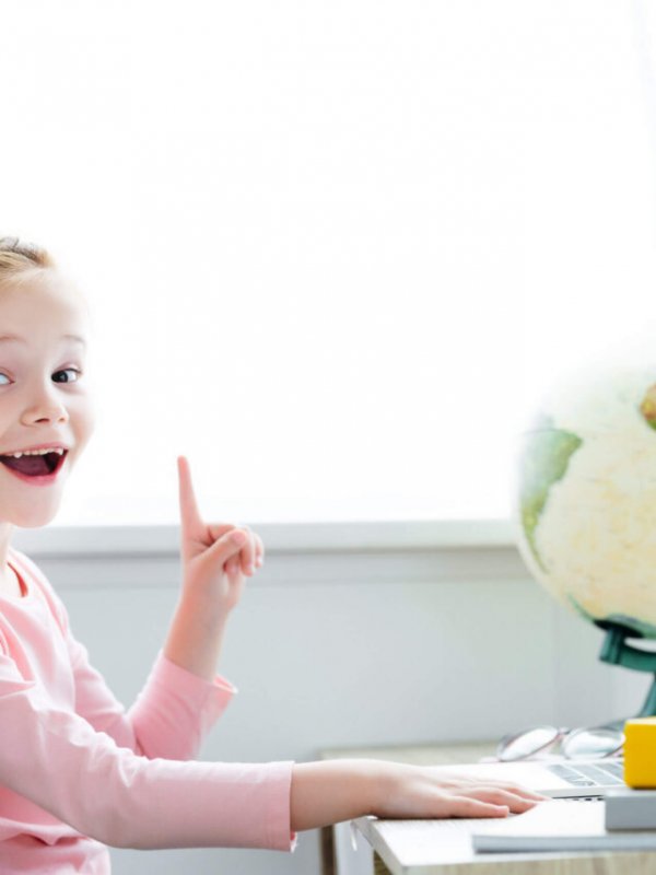 cheerful redhead child pointing up with finger and smiling at camera while studying with books and