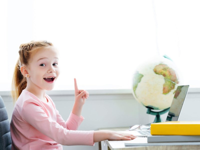 cheerful redhead child pointing up with finger and smiling at camera while studying with books and cheerful redhead child pointing up with finger and smiling at camera while studying with books and