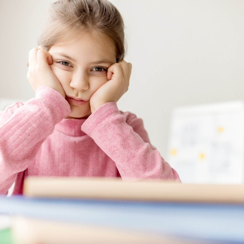 Reluctant schoolgirl touching her cheeks by hands while sitting at lesson