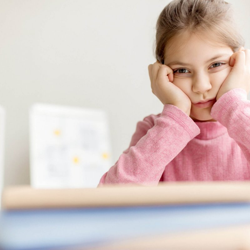 Reluctant schoolgirl touching her cheeks by hands while sitting at lesson